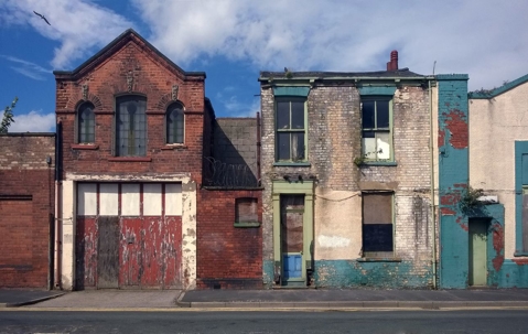 Derelict houses on a residential street with boarded up windows and decaying crumbling walls